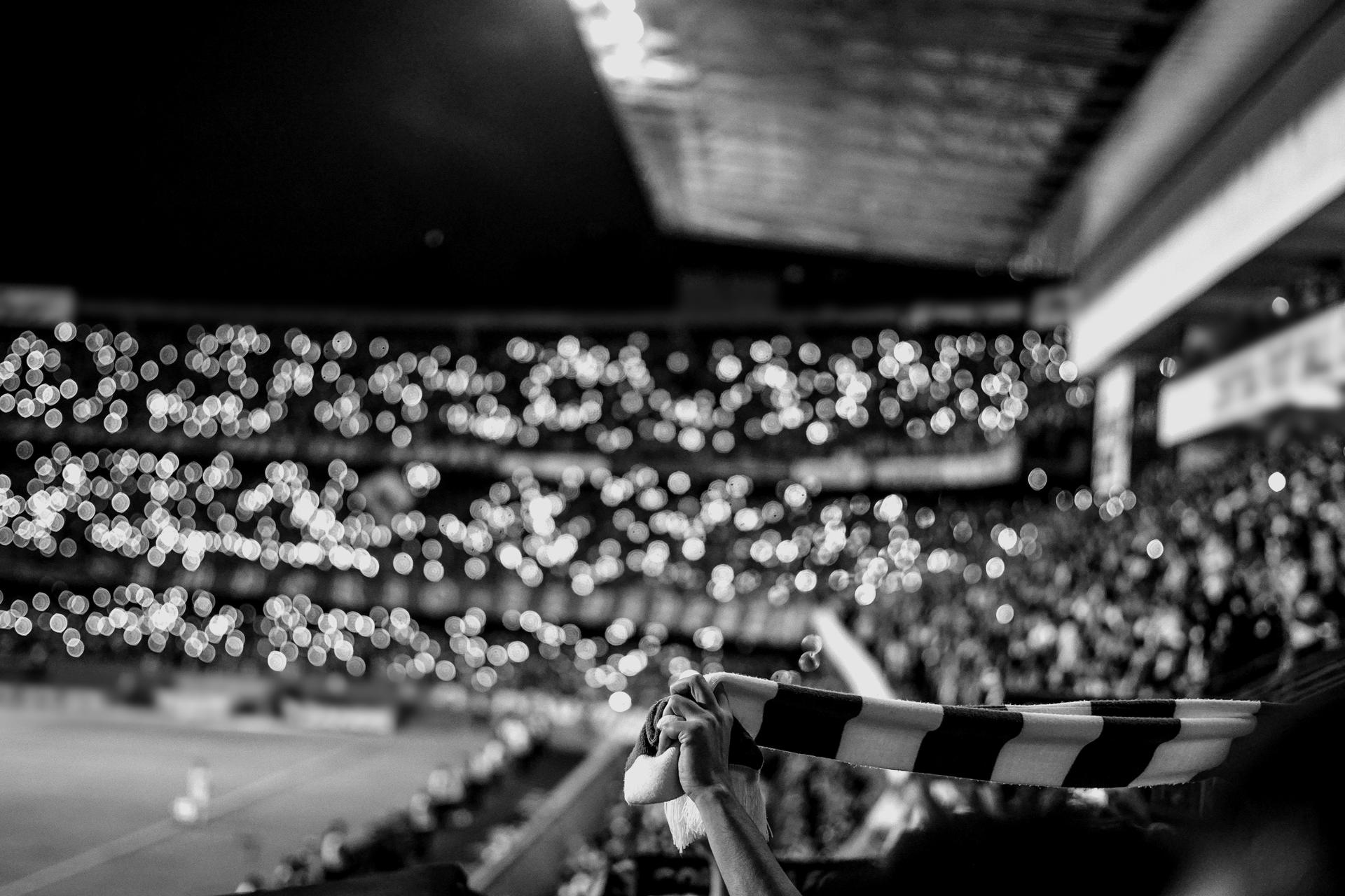 Fans raise a striped scarf in a stadium lit by thousands of phone lights